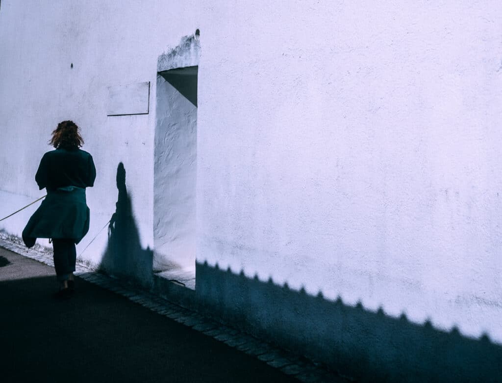 Eine Frau geht an einer weißen Hauswand entlang  und wirft Schatten